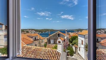 A coastal town with terracotta-roofed buildings, a clear blue sky, and a view of the sea.