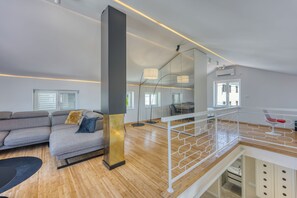 A modern living room with a grey sofa, a wooden floor, and a staircase with a white railing. - 1BR Star Wars Inspired Duplex Loft /w Sea View (Mali Losinj)