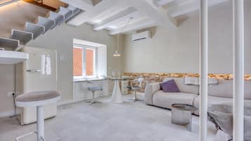 Ein modernes Interieur mit einer Treppe, einer Küchenzeile, einem Esstisch mit Stühlen, einer Couch und einem kleinen Tisch mit einer Vase.