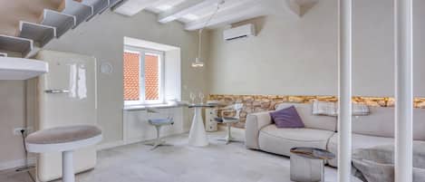 A modern interior with a staircase, a kitchen area, a dining table with chairs, a sofa, and a small table with a vase.