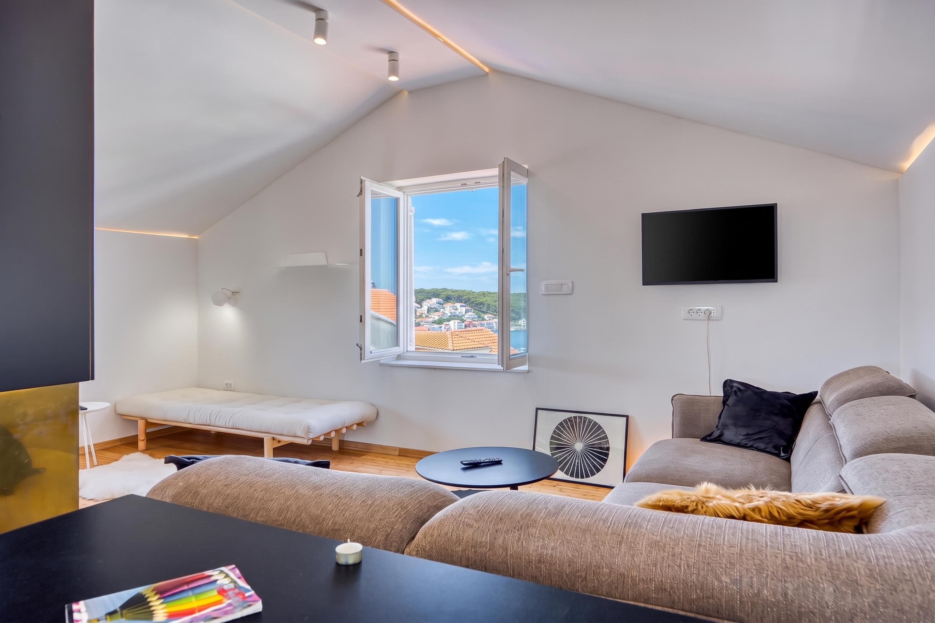 A modern living room with a loft bed, a flat-screen TV, and a view of a cityscape through a large window.