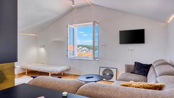 A modern living room with a loft bed, a flat-screen TV, and a view of a cityscape through a large window.