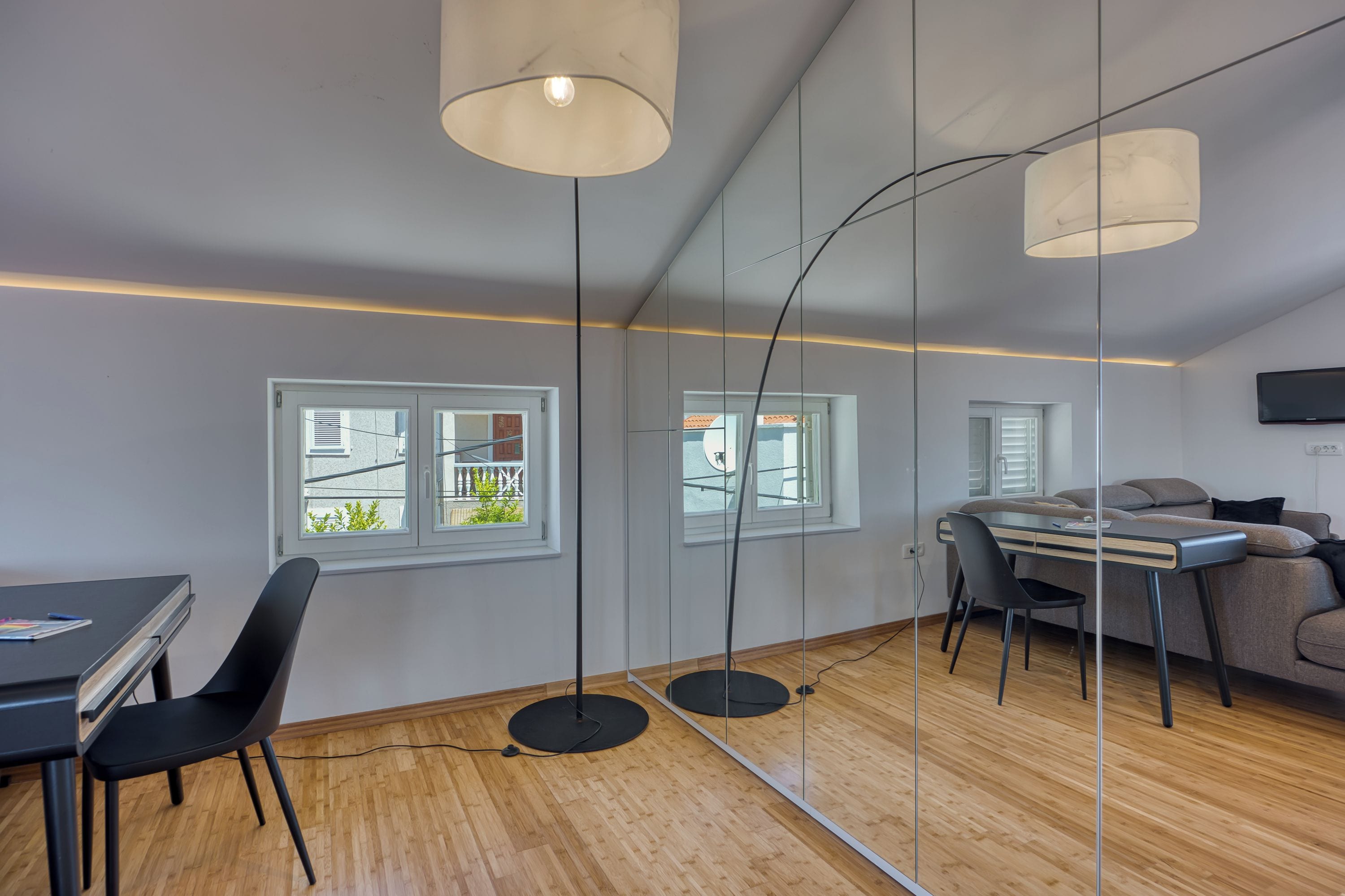 A modern living room with a dining area, large windows, and a flat-screen TV mounted on the wall.