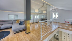 Una sala de estar moderna con un sofá gris, piso de madera y una escalera con barandilla blanca.