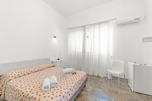 Une chambre d’hôtel équipée d’un lit, d’une chaise, d’un bureau, d’un climatiseur et d’une fenêtre avec des rideaux.