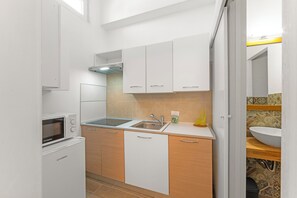 Eine kompakte Küche mit weißen Schränken, einer Mikrowelle, einem Spülbecken und einem kleinen Kühlschrank.