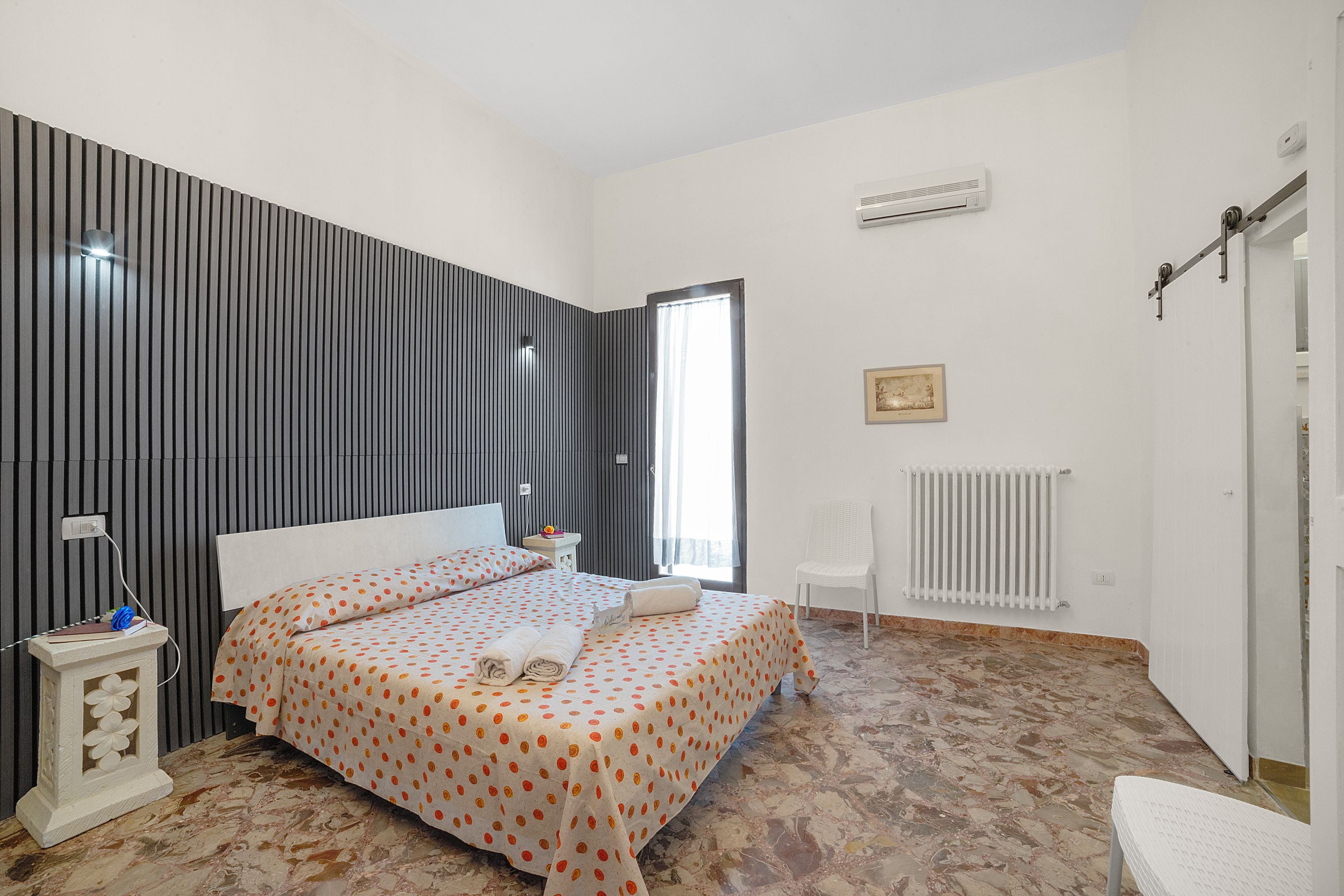 Un dormitorio con cama, mesitas de noche, radiador y ventana.