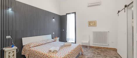 Un dormitorio con cama, mesitas de noche, radiador y ventana.