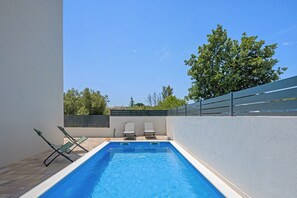 A rectangular swimming pool with two lounge chairs on one side and a tree in the background. - Villa Ana Pool & Terrace (Vodice)