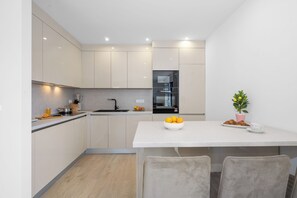 A modern kitchen with a white countertop, a sink, and a dining area with two chairs. - Villa Ana Pool & Terrace (Vodice)