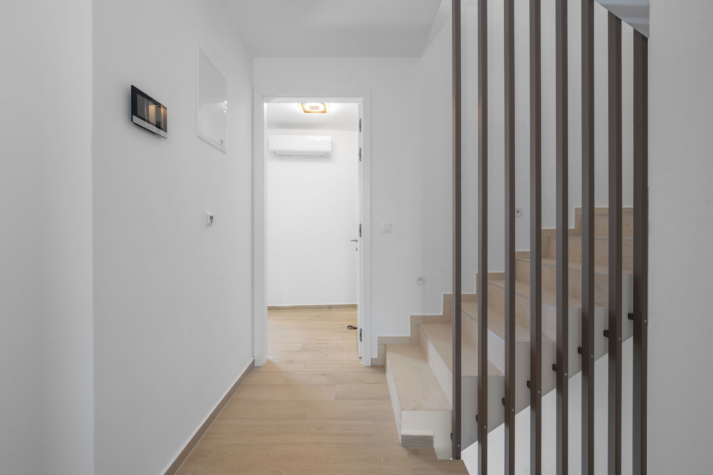 Un pasillo con una escalera de madera, paredes blancas y una puerta que da a otra habitación.