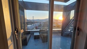 A balcony with a view of the sunset, a staircase, and outdoor furniture.