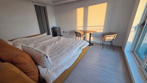 A modern hotel room with a large bed, a sofa, a small table, and chairs.