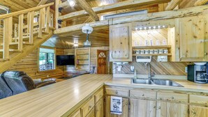 Interior de una cabaña de madera con área de cocina, escalera de madera y un cartel de bienvenida.