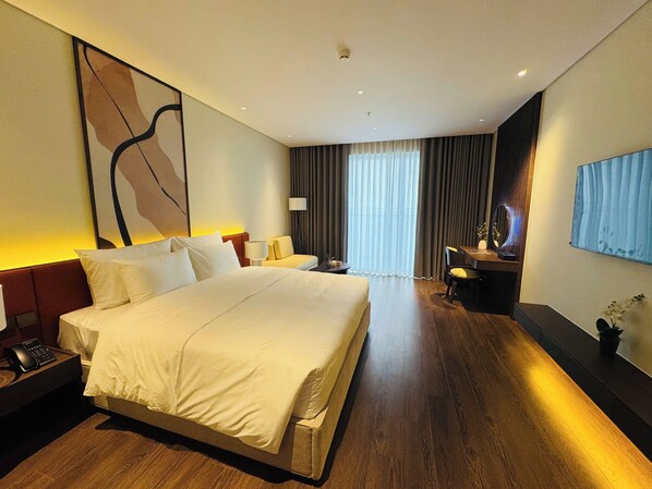 A modern hotel room with a large bed, bedside tables, a desk, and a large window with curtains.