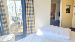 Et hotelværelse med en seng, et vindue med gardiner, udsigt til det fri og en dør til et andet rum.