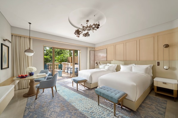 Habitación de hotel con dos camas, una zona de estar con mesa y sillas, un ventanal grande y un aplique de techo.