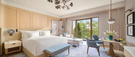 A modern hotel room with a large bed, a seating area with a table, and a balcony with a view.
