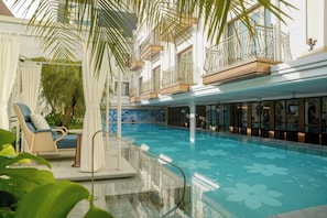 Una piscina con piso estampado, rodeada por un área techada con una silla y una mesa.