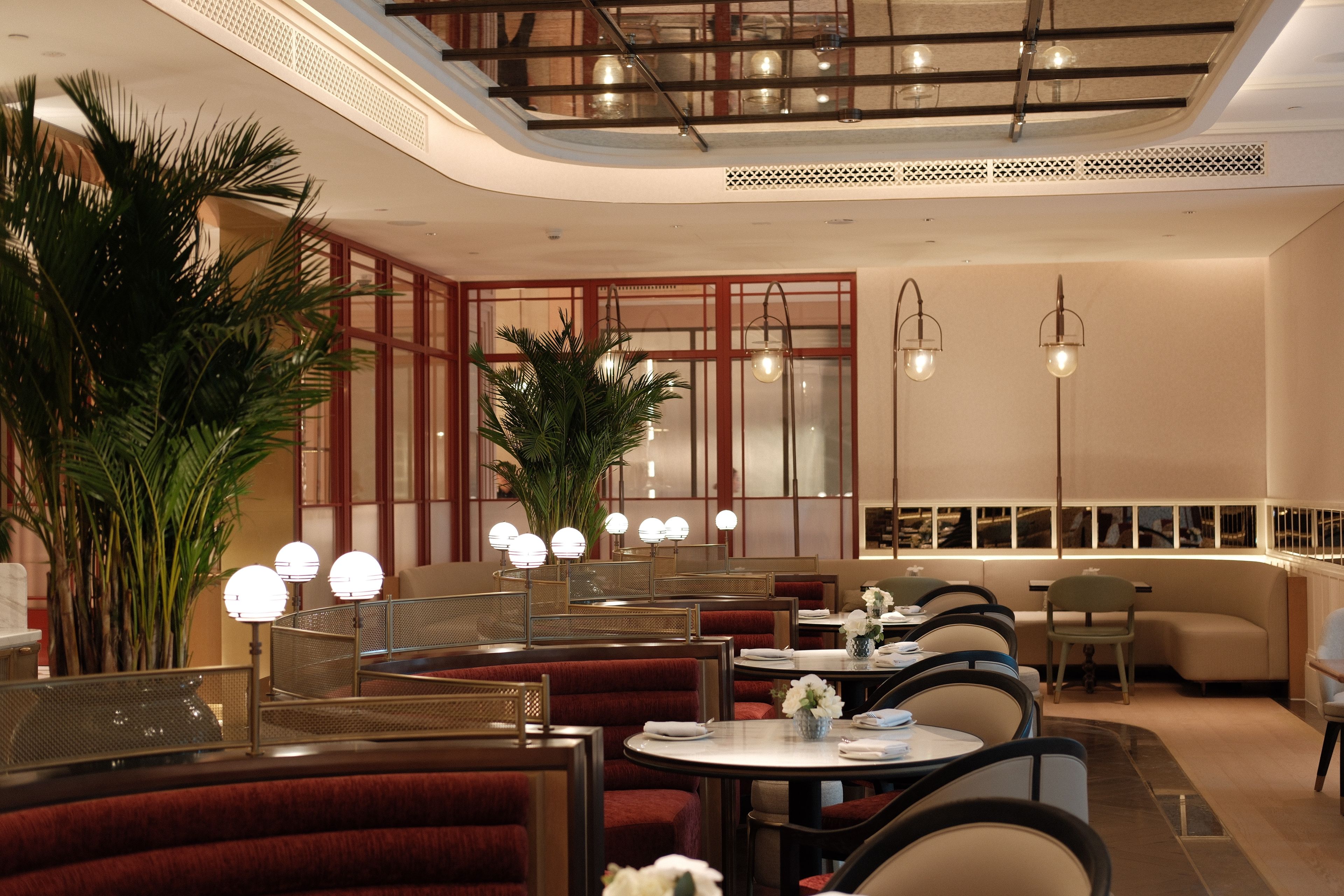 Een restaurantinterieur met ronde tafels, rode gestoffeerde zitbanken en hangende hanglampen.