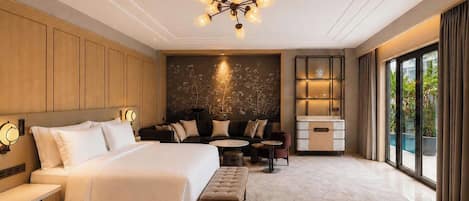 A modern hotel room with a large bed, seating area, and a view of greenery outside.