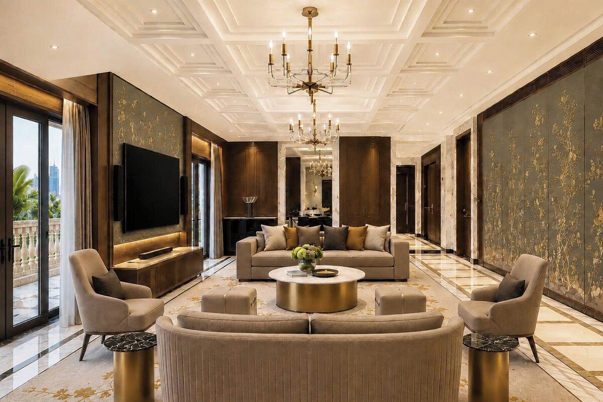 A spacious living room with a large sofa, a coffee table, and a TV. There are two armchairs and a fireplace. The room has a modern design with a chandelier and patterned wallpaper.
