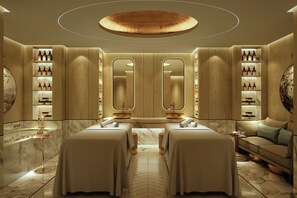 A spa room with two massage tables, wooden cabinets with shelves of bottles, and a large mirror. - The Theodore Hanoi (Hanoi)