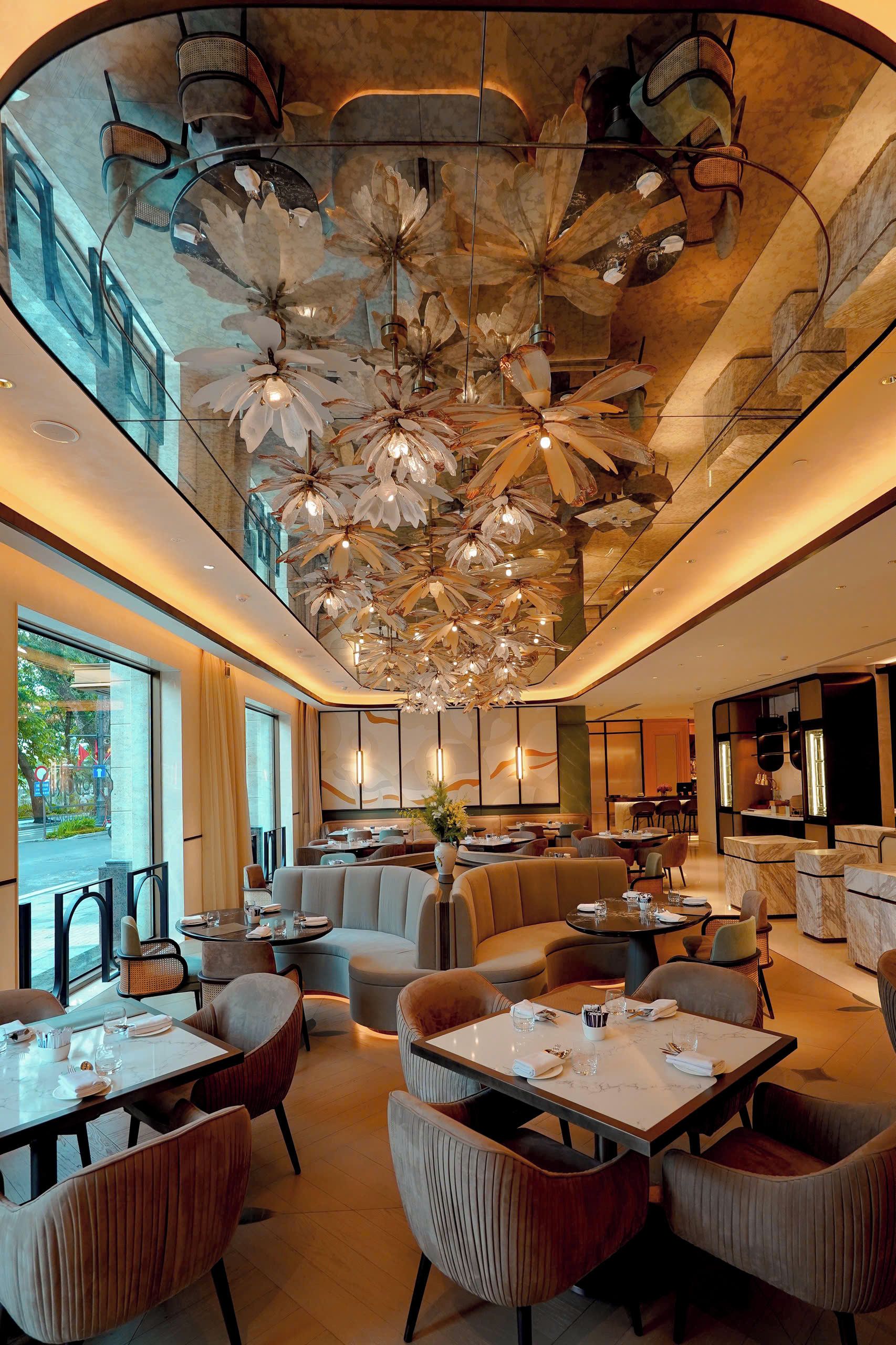 A modern hotel lobby with a high ceiling, large seating area, and a dining space.