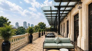 A rooftop terrace with a patterned floor, outdoor seating, and a city view. - The Theodore Hanoi (Hanoi)