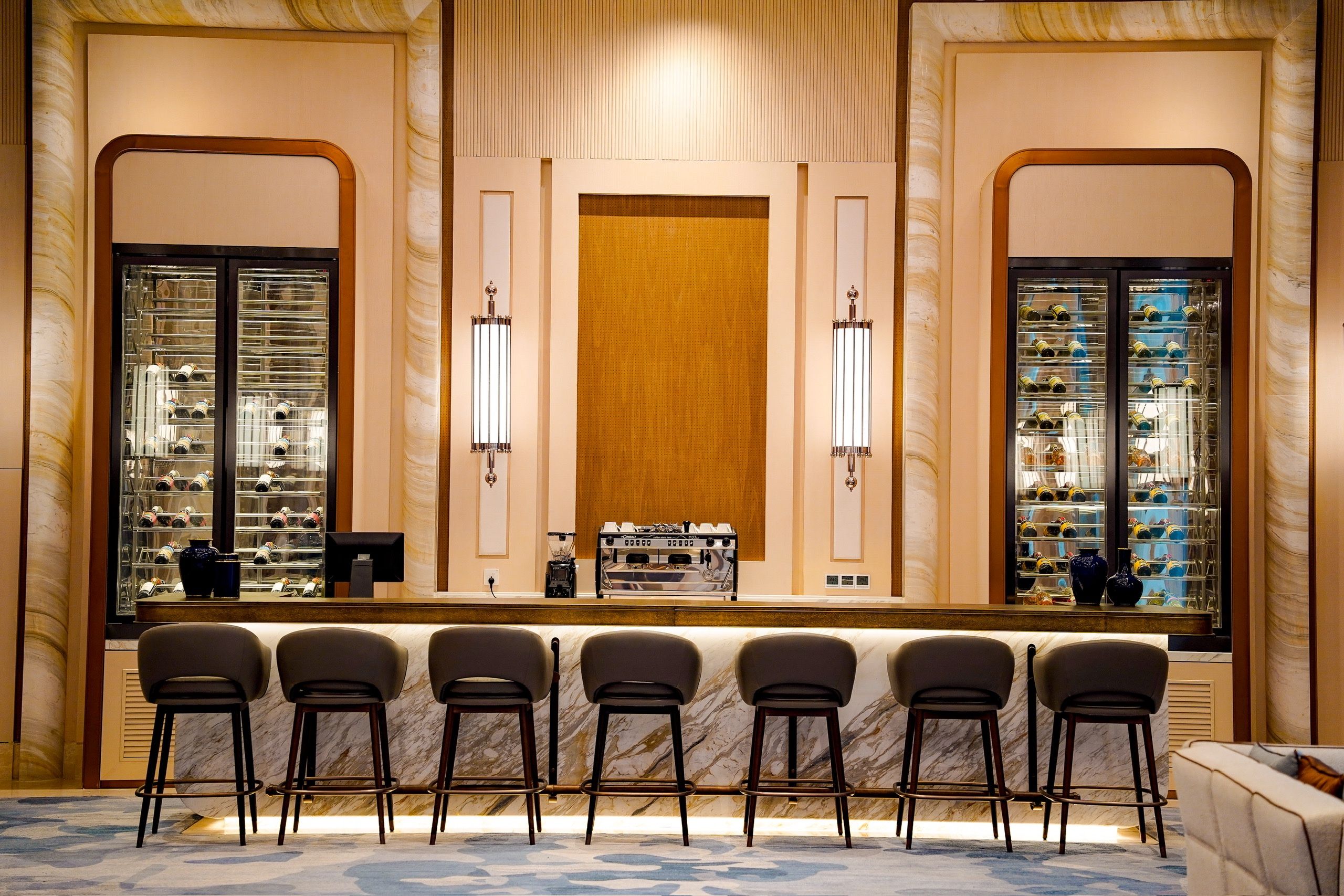 Een bar met een marmeren vloer, barstoelen en wijnrekken.