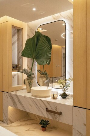 A bathroom with a marble vanity, a large mirror, and a potted plant. - The Theodore Hanoi (Hanoi)