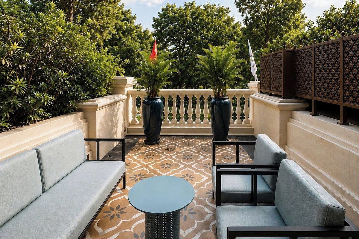 An outdoor seating area with sofas and a round table, surrounded by decorative plants and a patterned floor.