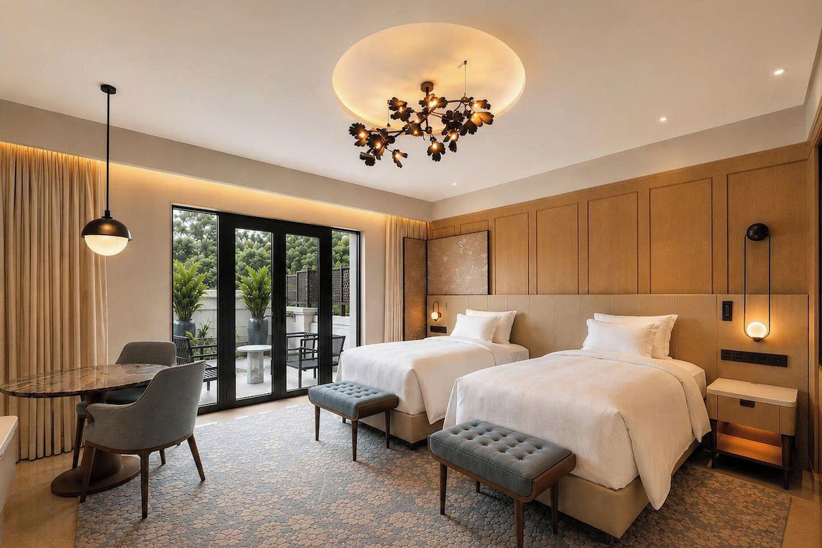 A hotel room with two beds, a dining area, and a view of greenery outside.