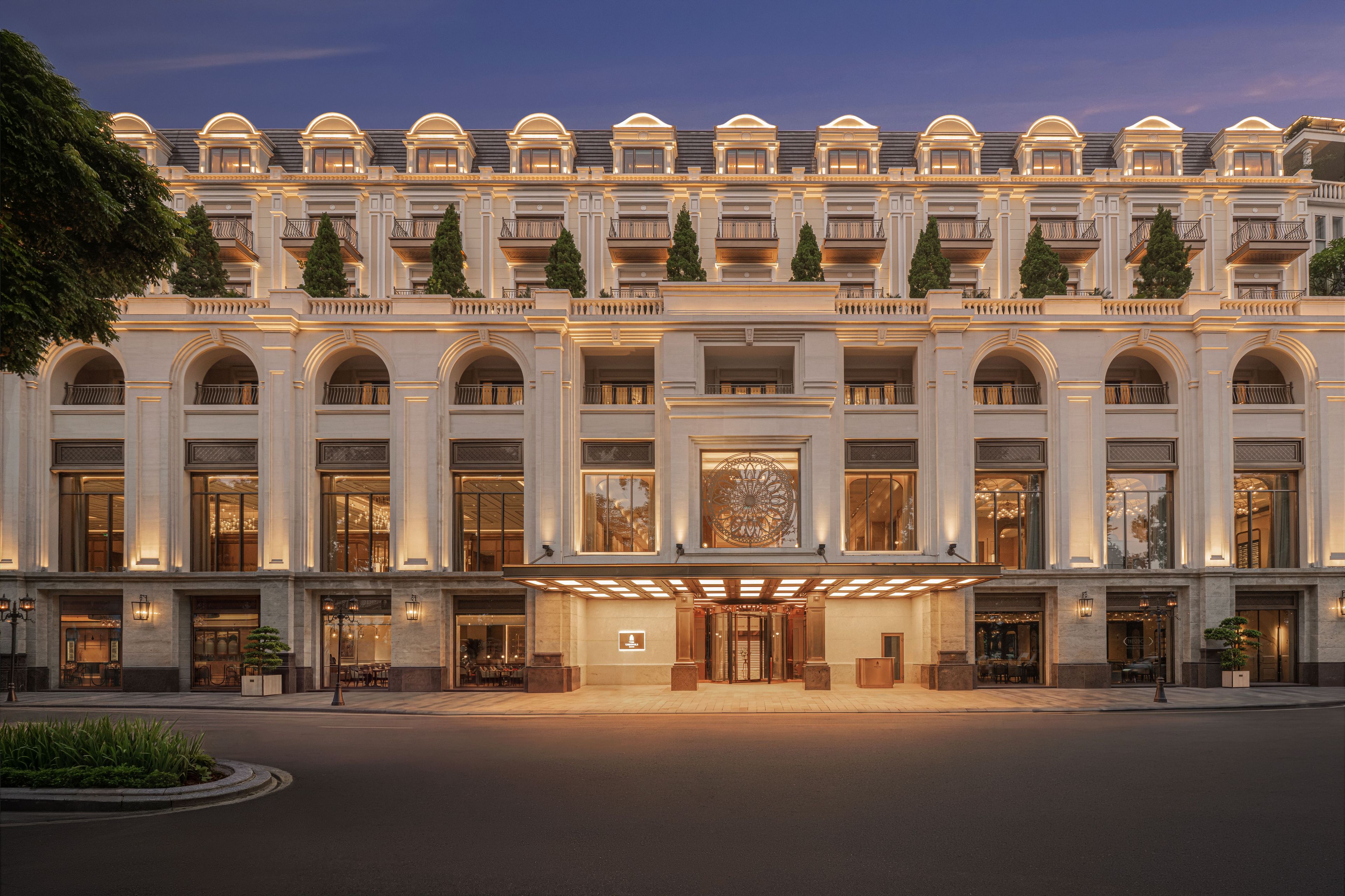 A grand hotel facade with multiple balconies, large arched windows, and a central entrance with a decorative glass door.