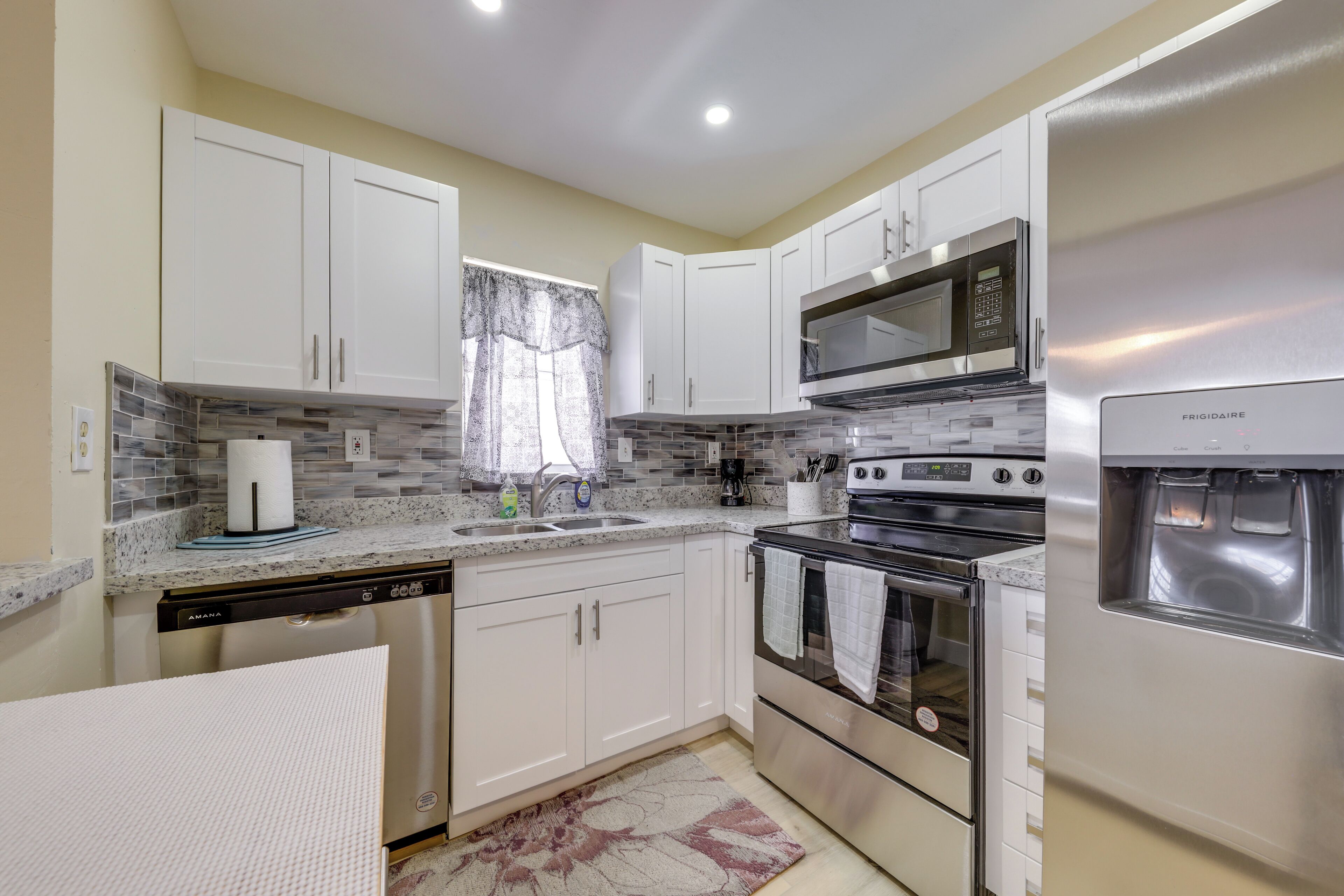 A modern kitchen with white cabinets, a stainless steel refrigerator, a built-in microwave, and a dishwasher.