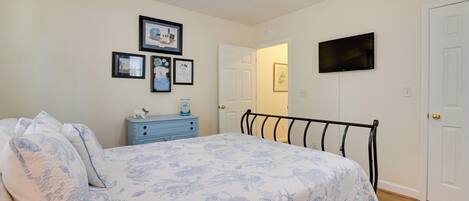 A bedroom with a bed, a ceiling fan, a dresser, a television, and framed pictures on the wall.