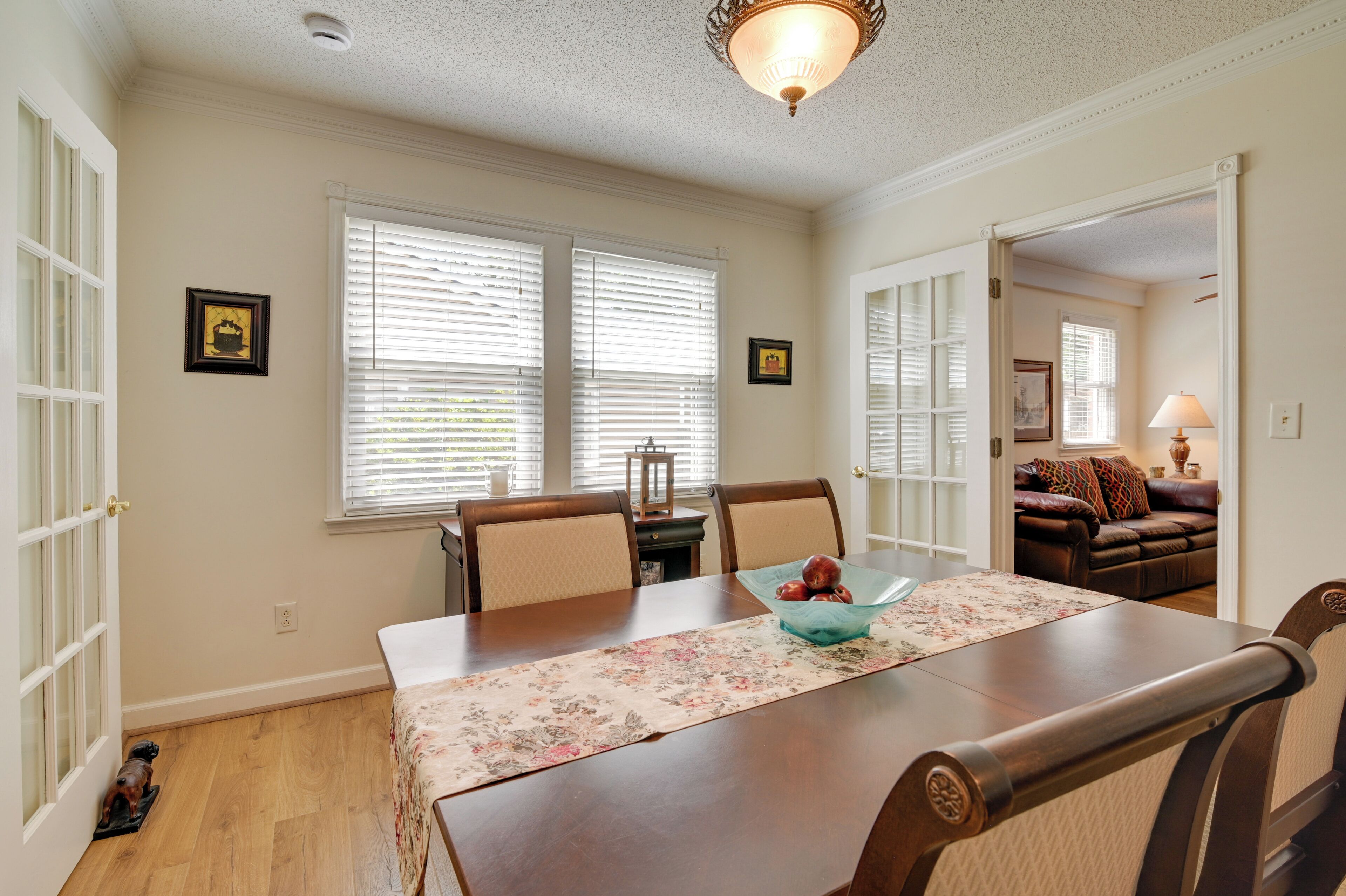 A dining area with a wooden table, chairs, a floral table runner, and a bowl of fruit.