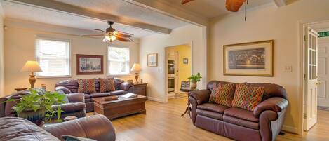 A spacious living room with leather sofas, a ceiling fan, and a dining area with a table and chairs.