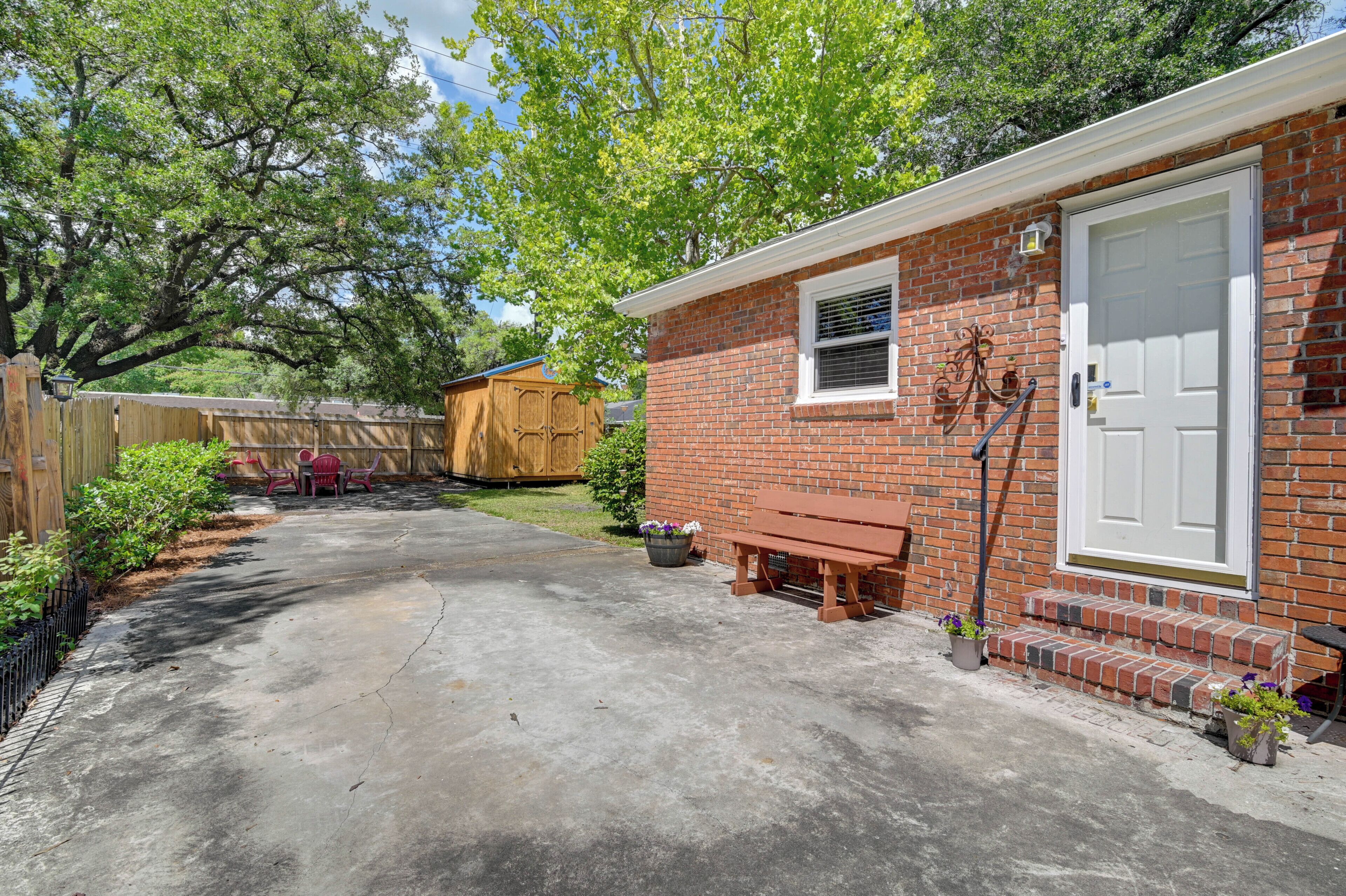A brick house with a front door, a small porch, and a wooden shed in the background.