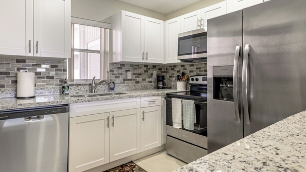 Una cocina moderna con armarios blancos, un refrigerador de acero inoxidable, un lavavajillas y un microondas.