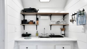 Cozinha compacta com armários brancos, pia e diversos utensílios e eletrodomésticos.