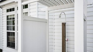 Exterior branco com porta de madeira, uma janela e um chuveiro de metal.