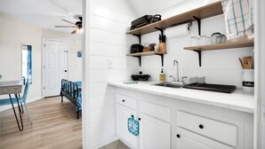 Uma cozinha moderna com armários brancos, prateleiras de madeira, uma pia e um ventilador de teto.