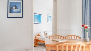 Ein Zimmer mit einem Bett, einem Esstisch mit Stühlen, einer Vase mit Blumen und gerahmten Bildern an der Wand.