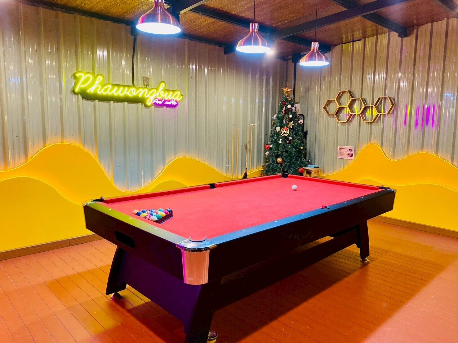 A pool table in a room with a neon sign, a Christmas tree, and hexagonal wall decorations.