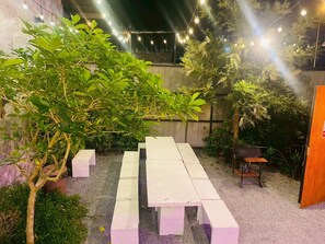 A patio area with a long white table, potted plants, and string lights. - Phawongbua Pool Villa (Songkhla)
