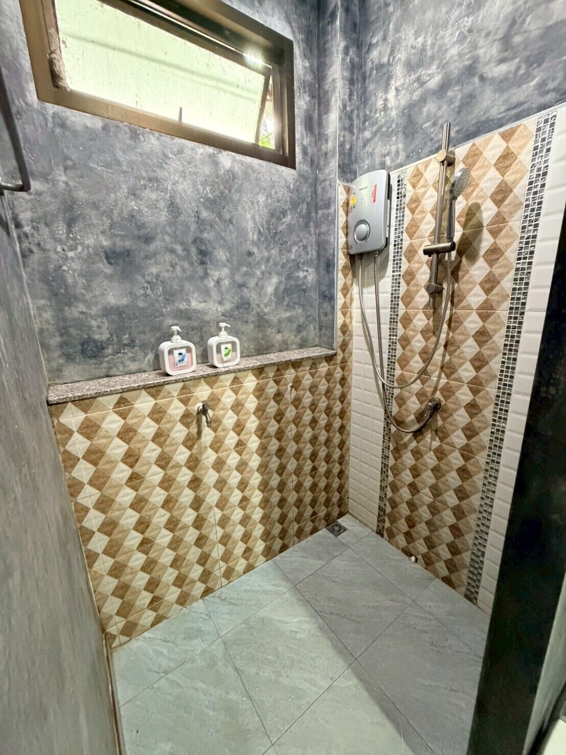 Un baño pequeño con ventana, ducha y dos dispensadores de jabón en la pared.