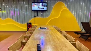 Een vergaderzaal met een lange tafel, stoelen, een televisie en een presentator.