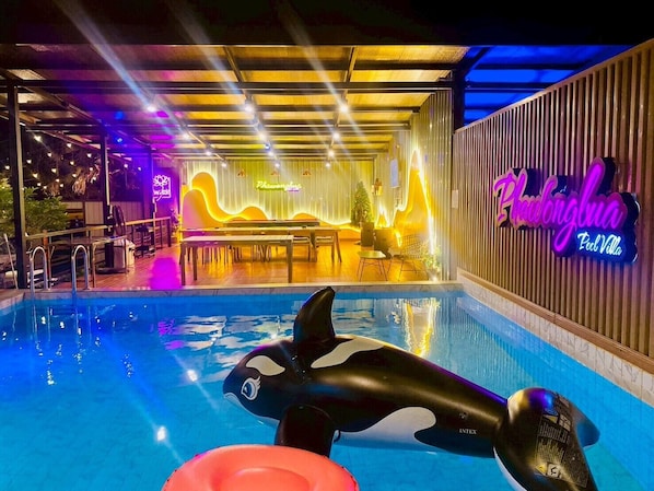 Una piscina interior con un flotador con forma de orca, un letrero de neón y una zona de bar.