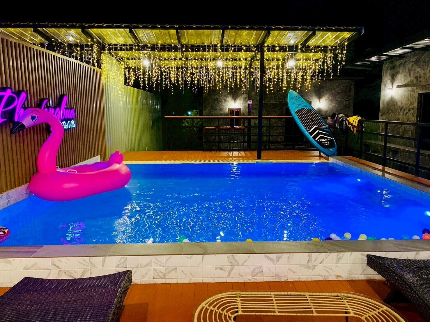 Una piscina con un flotador de flamenco rosa, una tabla de surf y un letrero de neón.